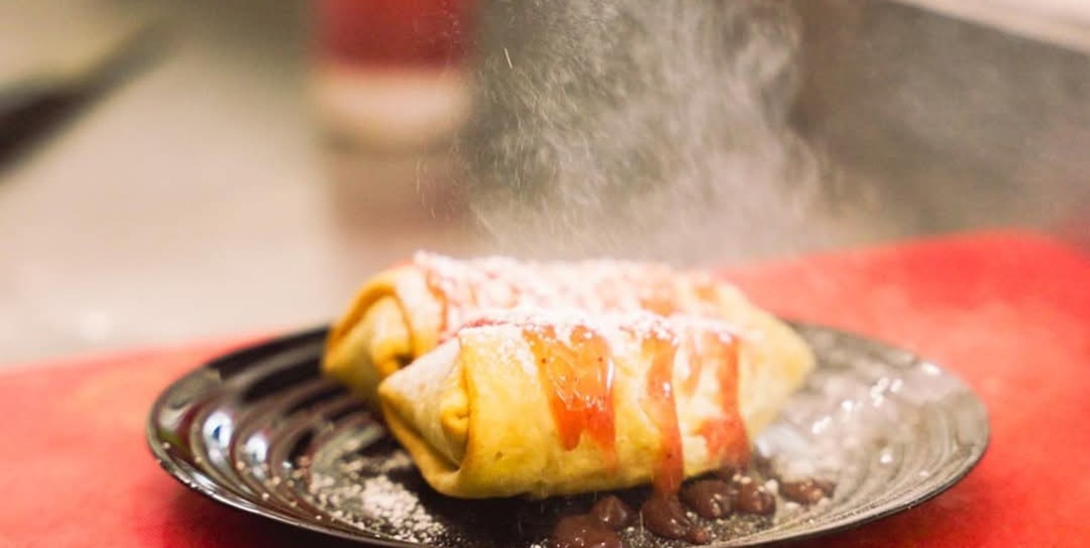 A plated breakfast burrito with sauce