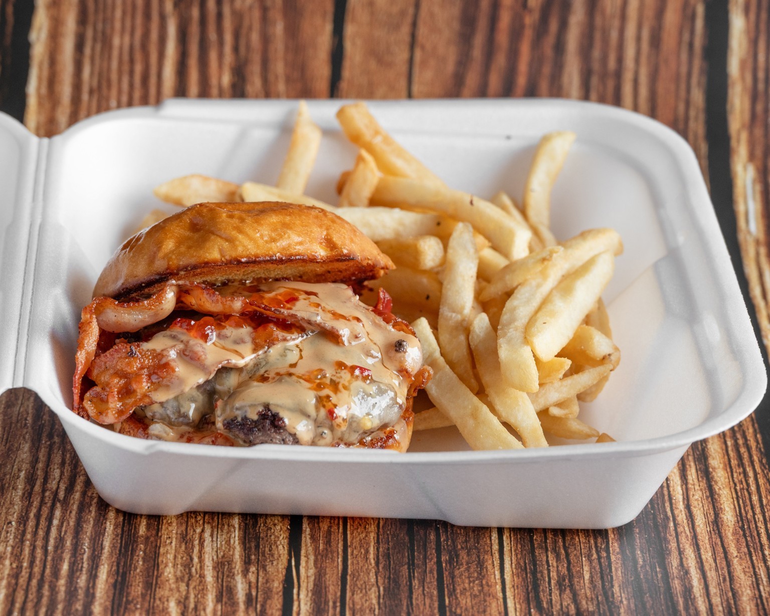 A stacked burger with melted cheese, bacon, and fries